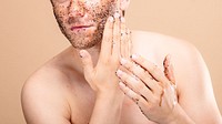 Caucasian man applying facial scrub. Close-up of white man with scrub on face. Skincare routine for men. Man applying face scrub. Self-care for men with scrub. Man with facial skin care.