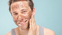 A man with a facial scrub smiles, applying exfoliating scrub. Skincare routine with facial scrub, exfoliating for healthy skin. Happy man enjoying skincare. Man with facial scrub on face, skincare.