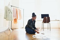 African American woman sitting on floor with fashion design sketch papers. African American woman focused on fashion work. African American woman working on floor of fashion design studio.