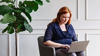 Woman red hair use laptop online working from home, modern casual room. Confident woman working with laptop on chair, focus on work. Woman working online in casual home, focus and type on laptop