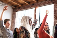 Woman in hijab and diverse group of people raising hands in a Seminar room setting, showing engagement and participation. Seminar room with large windows and brick walls.