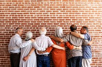 Group of senior people standing together, arms around each other, facing a brick wall. Diverse seniors, friendship, unity, community, togetherness, support. Senior diverse people supporting each other