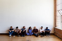 Group of diverse relaxed people sitting on the floor against a wall. Casual, relaxed, diverse group enjoying time together. Diverse group of people sitting on the floor on wooden floor.