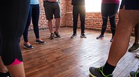 Group of people in athletic wear standing in a circle on wooden floor. Casual athletic shoes, diverse group, exercise setting, brick wall background. Diverse people exercising in circle at gym.