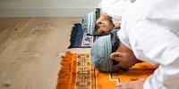 Two muslim men praying on rugs, wearing traditional attire and caps, engaged in prayer. Focus on prayer, traditional attire, and spiritual practice. Muslim men praying during Ramadan.