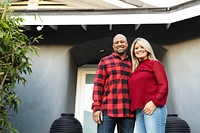 Smiling diverse couple standing in front of a house. Diverse man and woman in red shirt smiling in front of the house. Happy couple enjoying their home. Couple standing in front of their home happy.