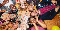 Group of diverse friends celebrating, lying on floor with confetti. Smiling, joyful, diverse group enjoying party. Happy, festive, diverse celebration. Diverse friends celebrating at New Year's party.