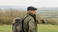 Senior man hiking outdoors with backpack. Senior man backpack travel, enjoying nature landscape. Scenic view with hiker. Outdoor adventure for senior man in countryside. Senior man travel in nature