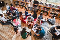 Diverse group of students studying in a library, reading books, and discussing. Students in a library setting, engaged in study and discussion. High school students reading in library.