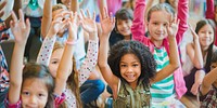 Group of diverse children raising hands in classroom. Smiling kids, eager to learn, show enthusiasm. Multicultural classroom, diverse students, happy faces. Cute little diverse kids smiling at camera.