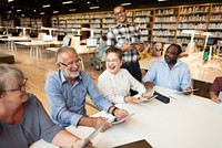 Group of diverse adults in a library, smiling and using tablets. Engaged in discussion, diverse group enjoying technology in a library setting. Diverse senior adults in group therapy at library.