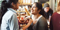 Two people smiling and chatting in a cozy cafe, enjoying a friendly conversation. Warm atmosphere with pastries and coffee in the background. Indian women mingle together at a bar and social event.