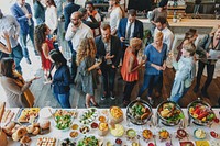 A vibrant gathering of diverse people enjoying a buffet. Men and women of various ethnicities socialize, savoring delicious food and drinks at a lively event filled with laughter.