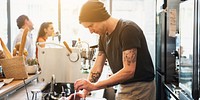 Barista making coffee in a cafe, wearing a beanie and apron. Sunlight filters in. Coffee preparation, barista skills, and cafe atmosphere are highlighted. Barista in coffee shop.