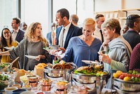 A diverse group of people enjoying a buffet at a social event. Men and women of various ethnicities engage in conversation while savoring delicious food at the buffet. Corporate event with buffet