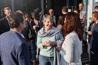 Group of diverse adults socializing outdoors, holding coffee cups. Casual gathering with men and women engaged in conversation, enjoying a sunny day. Diverse people mingle in social event outdoors.