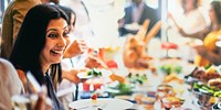 A joyful South Asian woman enjoys a vibrant buffet at a social gathering. The South Asian woman smiles brightly, surrounded by delicious food and happy guests at the event.