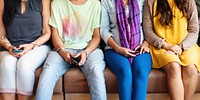 Four diverse people sitting on bench, holding phone, social network connection. Diverse group of people in casual clothes with mobile phone, socialize while sitting on bench. Diverse people with phone