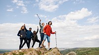 Group of hikers on a rocky peak, celebrating with trekking poles. Diverse group enjoying hiking, adventure, and nature. Clear sky and scenic view in the background. Happy friends on a hike.