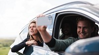 Group of friends taking a selfie from a car. Smiling people enjoying a road trip. Friends capturing moments on a road trip. Happy friends on adventure. Two people outdoors vacation with sky landscape.