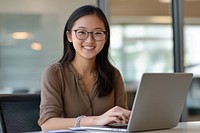 Asian woman sitting at her desk glasses laptop working.