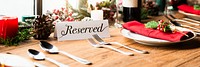 Festive table setting with reserved sign, red napkins, and candles. Holiday decor with reserved sign, pinecones, and red accents. Elegant reserved table setup. Christmas family dinner table.