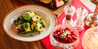 A plate of roasted Brussels sprouts with garlic on a wooden Christmas table. The dish is accompanied by a bowl of pomegranate seeds and salt and pepper shakers. Sides on table for Christmas dinner.