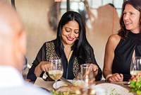 A joyful South Asian woman enjoys a meal at a dinner table, showcasing her vibrant attire. The South Asian woman smiles, savoring the moment with friends, creating a warm dining experience.