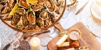 A platter of fresh oysters with lemon, surrounded by cheese and candles. Oysters and lemon, seafood feast. Oysters are the highlight of this elegant setting. Festive New Year gala dinner with oysters.