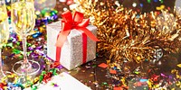 Festive celebration with a gift box, red ribbon, and colorful confetti. Sparkling decorations and a wrapped present create a joyful party atmosphere. Festive table with gift and party decorations.