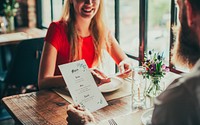 Couple having a lunch date in a restaurant. A woman in a red shirt smiles at a restaurant table. Menu, dining, and flowers create a cozy atmosphere. Restaurant, menu, and dining scene.