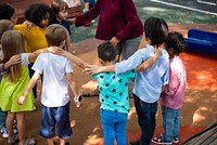 Children in a circle, arms around each other, diverse group, outdoor play, teamwork, unity, diverse children, outdoor fun, teamwork, unity, diverse group. Diverse school kids at playground.