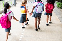 Four young girls with backpacks walk together on a path. School uniforms, backpacks, and friendship are highlighted in this cheerful scene. Cute little kids with backpacks in school.