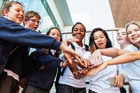 Group of diverse students in uniforms, hands together in unity. Smiling teens, teamwork, and friendship. School setting, diverse group, unity in action. Diverse students in team at school.