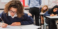 Students in a classroom taking a test. Focused students writing. Classroom setting with desks and papers. Diverse group engaged in exam. Girl in exam at school.