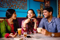 Three Indian people enjoying coffee and tea at a cafe. Smiling friends, diverse group, casual setting. Warm drinks, happy conversation, relaxed atmosphere. Indian friends chatting at cafe.