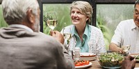 Group of older adults enjoying a meal together. Smiling woman with short gray hair. Diverse group sharing food, laughter, and conversation at a table. Happy friends celebrating with wine for lunch.