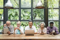 Diverse group of seniors using devices. Elderly men and women with tablets and laptops. Multicultural seniors enjoying technology together indoors. Senior people using digital devices and social media