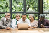 Diverse group of seniors enjoying time together. Seniors laughing, seniors using a laptop, seniors bonding. Happy seniors in a cozy, green setting. Senior people using digital devices and social media