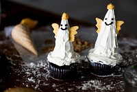 Two Halloween cupcakes with ghost decorations. Ghost cupcakes with white frosting and cookie wings. Halloween treats with ghostly designs and spooky decorations. Cute holiday cupcakes.