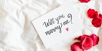 Romantic proposal card with 'Will you marry me?' text, surrounded by red rose petals on a white bed. Perfect for engagement, proposal, or romantic occasions. Marriage proposal on card with roses.