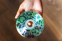 Hand holding a CD with doodles. Retro CD features various doodles, including hearts, stars, and aliens. Artistic retro music CD design with creative doodles.