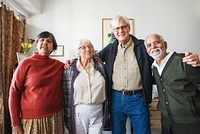 Group of four older adults smiling indoors. Two women and two men, diverse ethnicities, wearing casual clothing, standing together in a bright room. Diverse senior friends in retirement home.