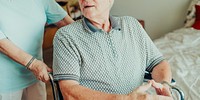 Elderly man in a wheelchair assisted by a caregiver. The caregiver helps and supports for the elderly man in a home setting. Retirement home service. Elderly in retirement home.