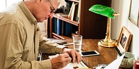 Elderly man writing at a desk, focused on paperwork. The man, with white hair, is working diligently. Desk, paperwork, and writing are key elements in this scene. Elderly man daily life photo.