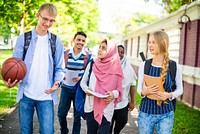 Diverse group of students walking outdoors, carrying books and a basketball. Young men and women, various ethnicities, enjoying a sunny day on campus. Diverse students walking in a park.