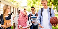 Diverse group of students walking outdoors, holding books and a basketball. Young adults, mixed ethnicities, enjoying a sunny day on campus. Diverse students walking in a park outdoor.