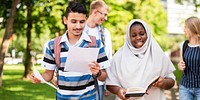 Diverse group of students walking outdoors, holding papers and books. Young adults, studying together, enjoying a sunny day on campus, engaged in learning. Diverse students walking in a park.