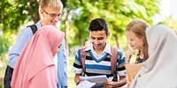 Group of diverse students studying outdoors, discussing notes. Students learning, sharing ideas. Diverse group enjoying collaborative study session. International students and friends at schoolyard.