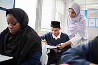 Muslim teacher in hijab assists students in classroom. Diverse classroom with attentive students. Education and learning environment with engaged students and teacher. Education and learning.